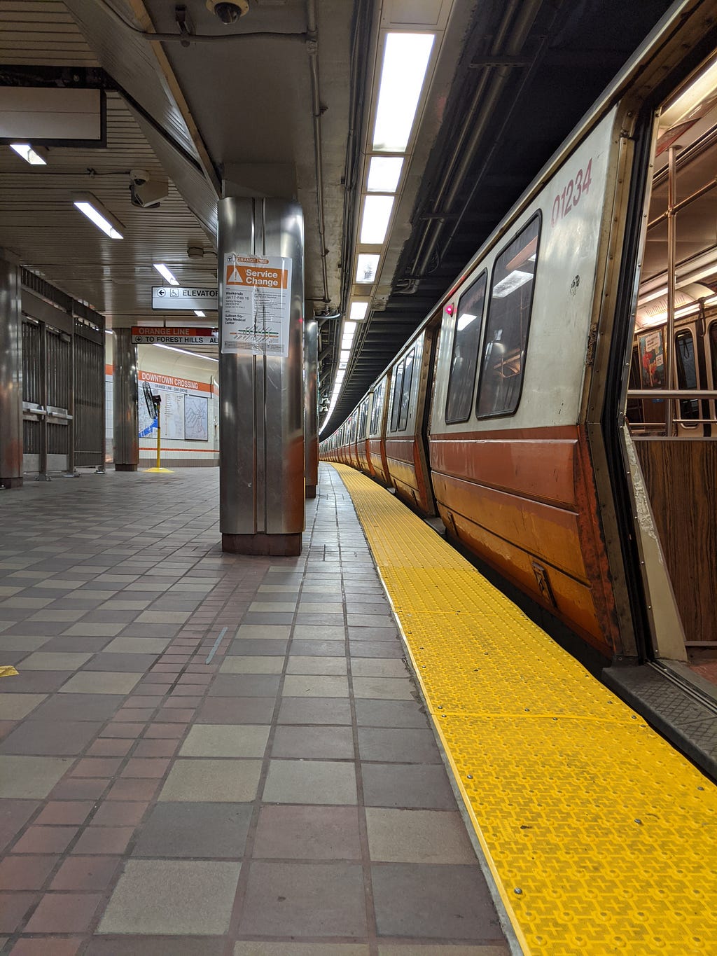 An Orange Line train waits at Downtown Crossing with doors open. There is a row of large pillars down the platform.