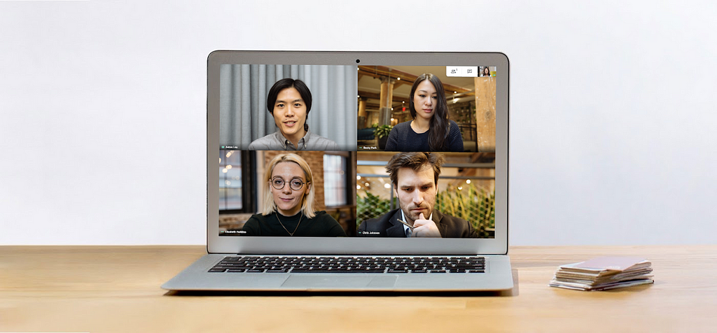 A laptop on a desk features a videoconference of 4 people