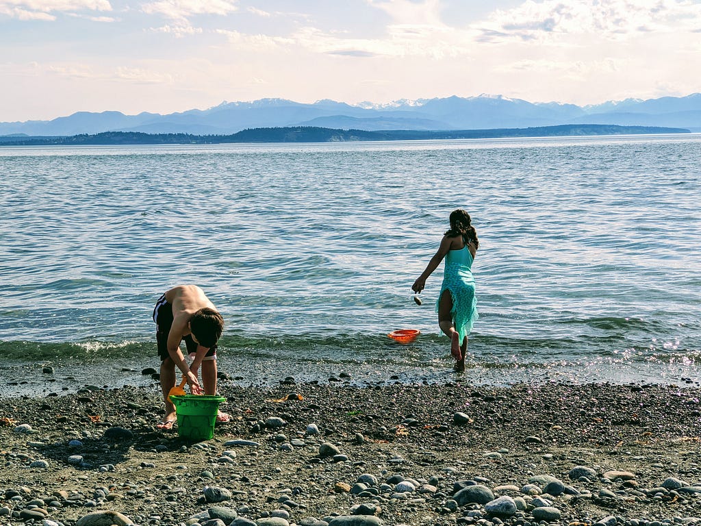 Two children playing in rocks and sand at the water’s edge.