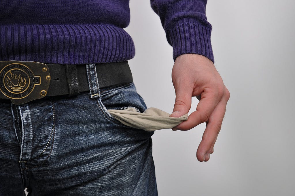 Person in sweater and jeans with belt turning their pocket inside out to show a lack of money.