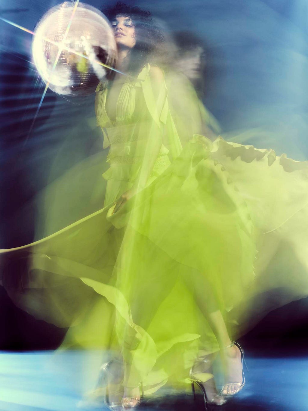 Blurred image of model in yellow dress dancing around a glitterball