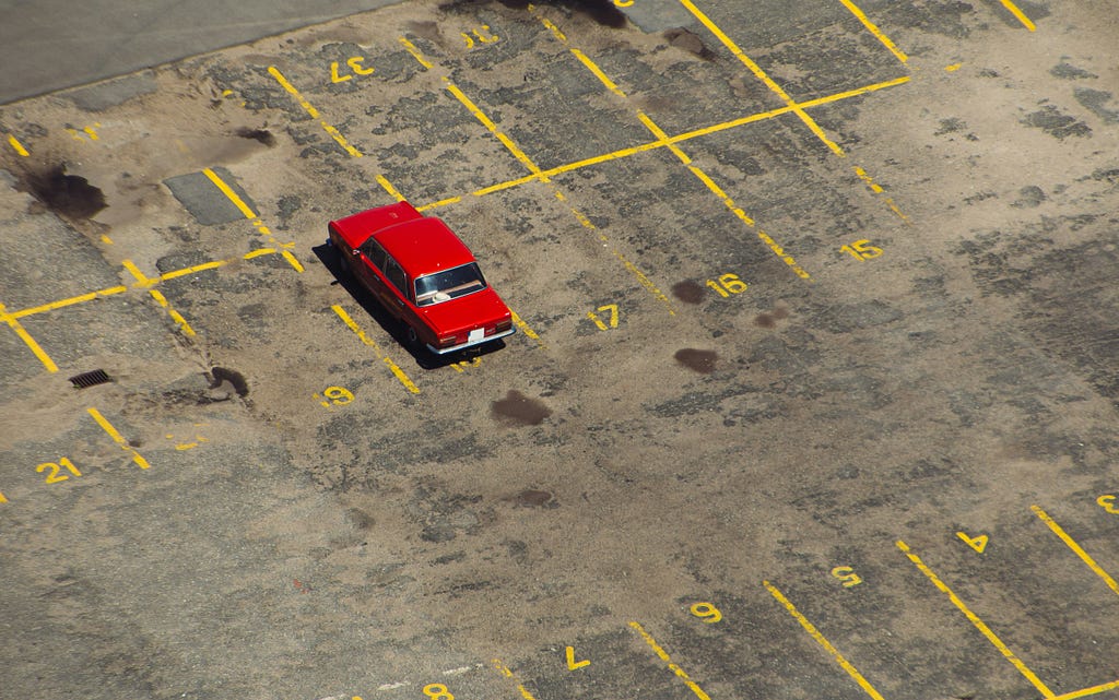 A photo of a single red car in an otherwise empty parking lot
