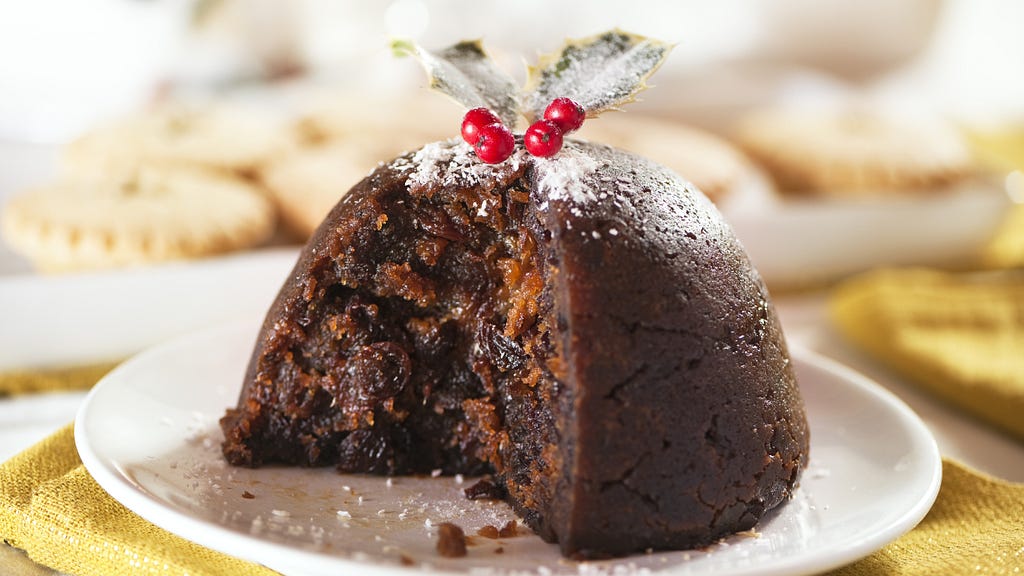 a fig pudding on a white plate, topped with powdered sugar and holly