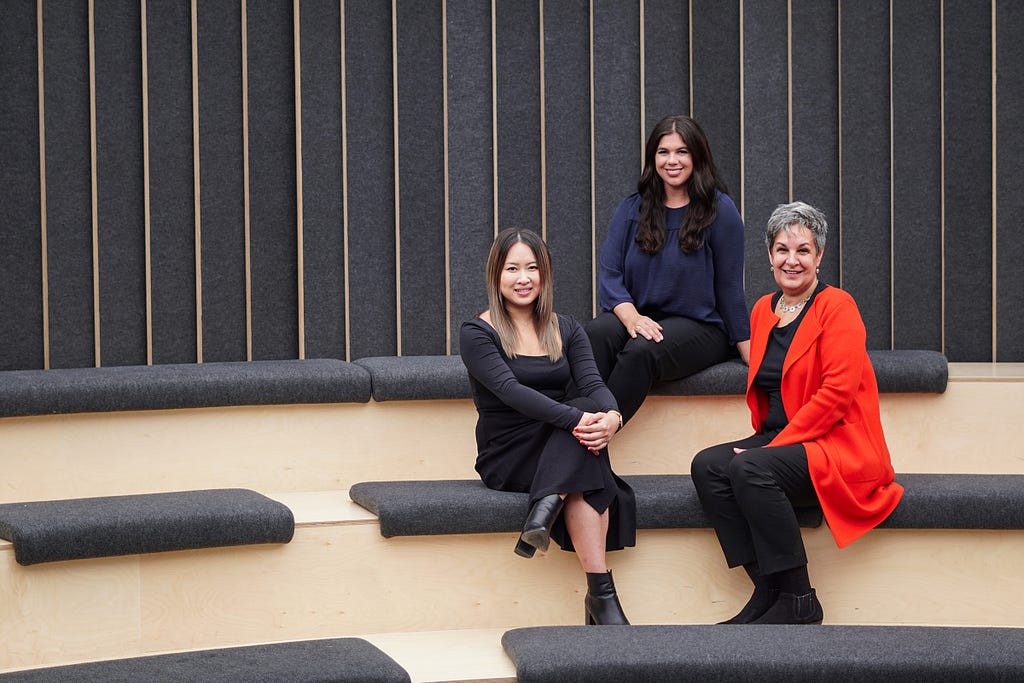 Three women sitting in a small auditorium smiling