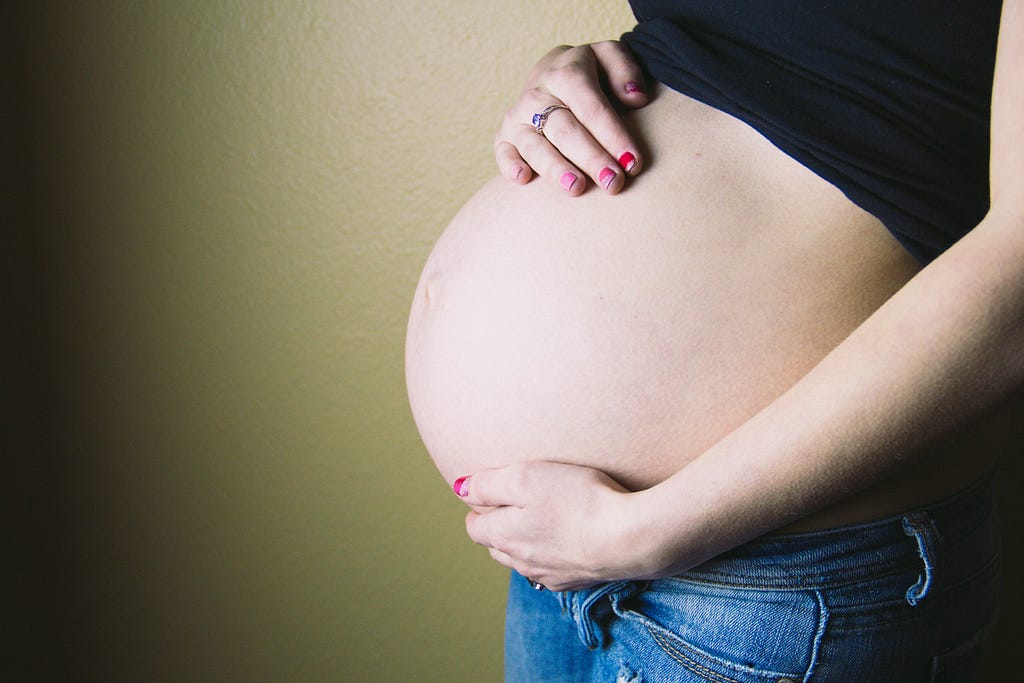 A pregnant woman, holding her belly.