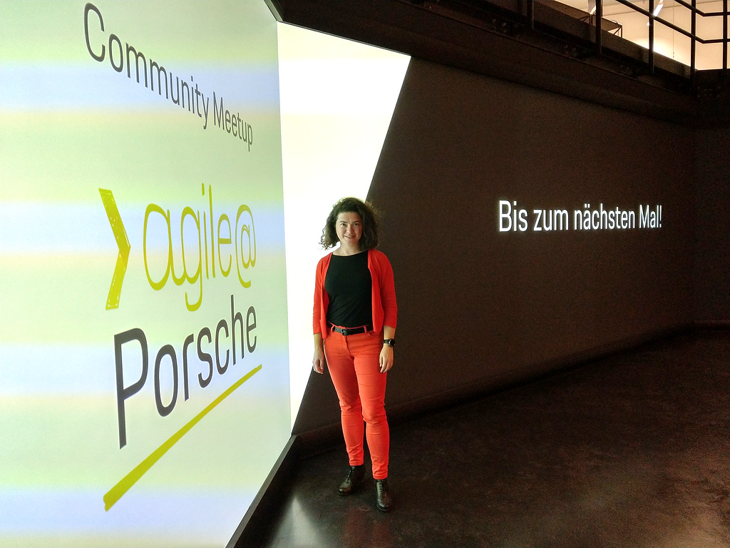 Woman in red outfit standing in front of a large digital wall with agile@Porsche written on the left