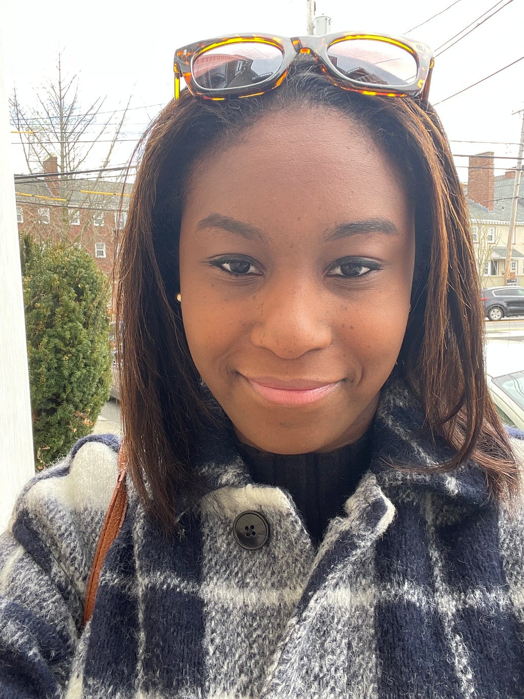 Headshot of Natalie Cantave looking directly at camera, wearing plaid jacket and sunglasses on her head