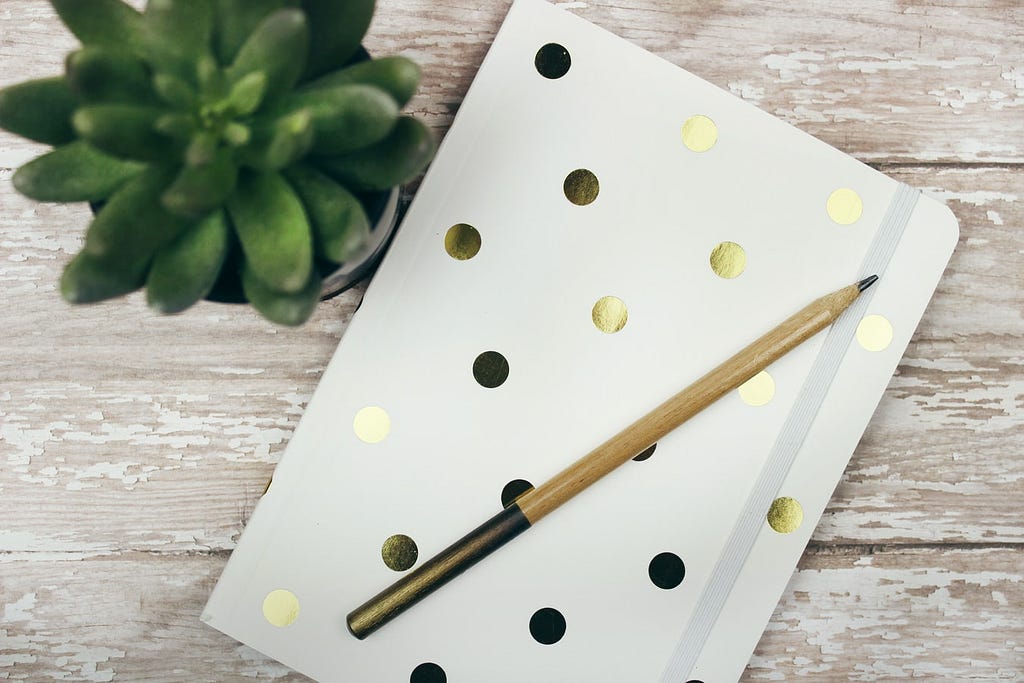 A white notepad with gold polka dots, placed next to a succulent on a wooden table.