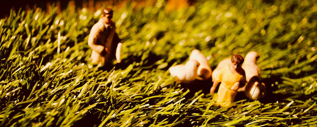 Small plastic models (of a man, a woman and some chicks) walk through long grass.