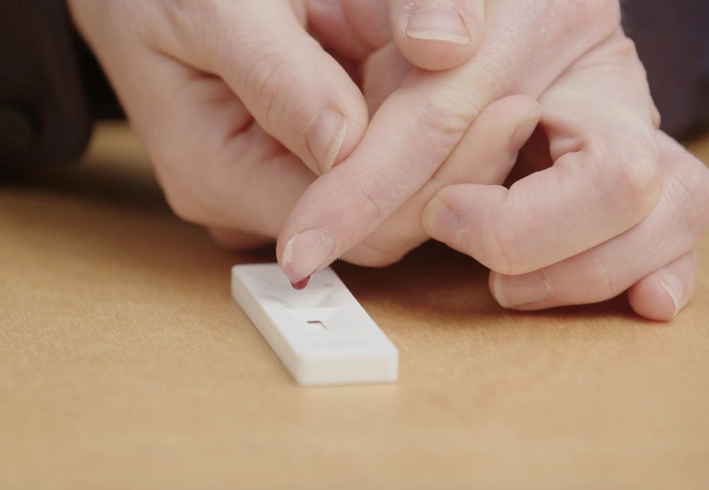 photo of finger that has just been pricked being squeezed to release a drop of blood