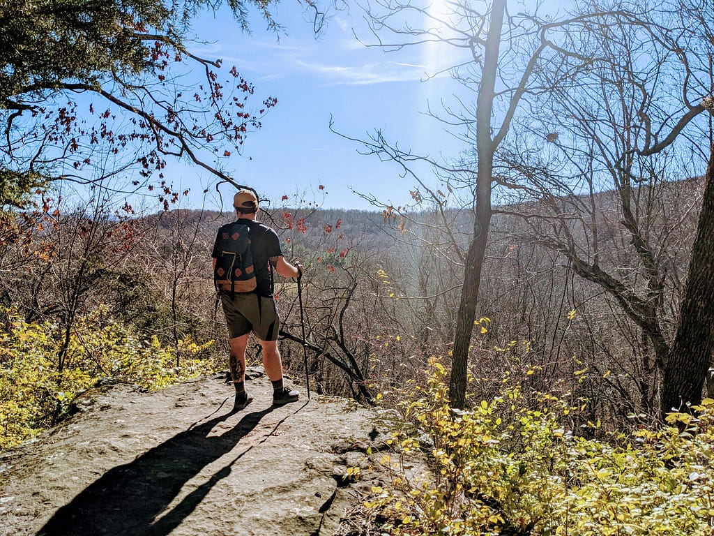 A hiker holding trekking poles stands on a rocky outcropping.