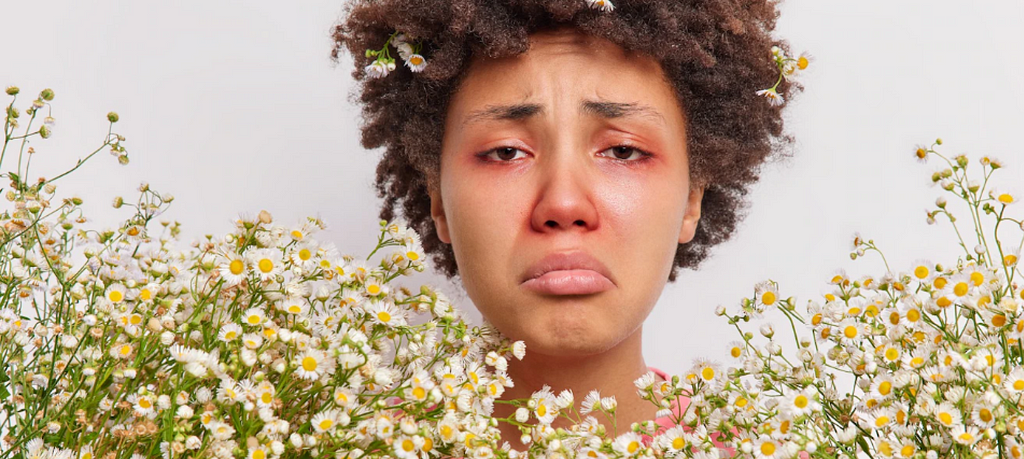 Mujer con síntomas de alergia rodeada de flores