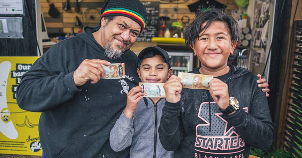 A man and two tama (boys) holding five dollar bills and smiling to camera