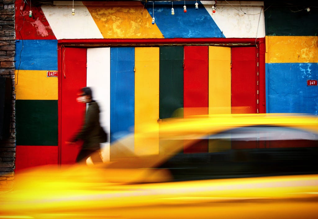 Man in black jacket walking beside red, blue and yellow building