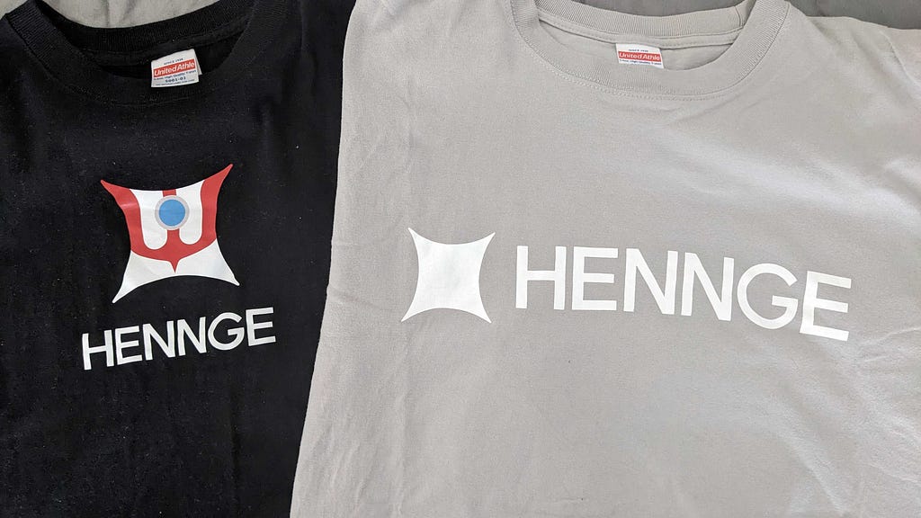 A black HENNGE Ultraman logo tee and a plain gray logo tee