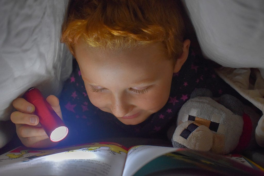 Child reading with a flashlight