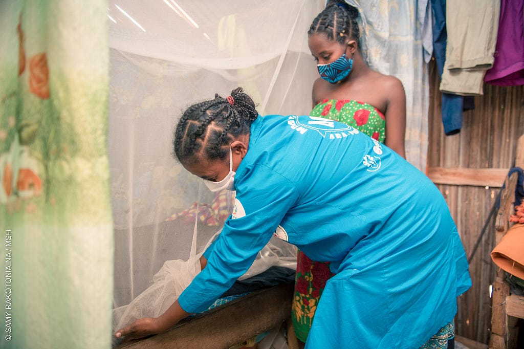 A community health volunteer shows a young woman how to properly tuck a mosquito net under her mattress