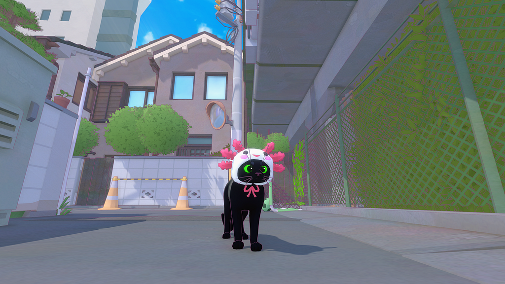 A black cat with green eyes facing the camera, wearing an axolotl hat tied around its head with string tied in a bow under its chin. The axolotl is a light white-blue, with the fins a vibrant pink. The cat is standing in a road with traffic cones and a house in the background, with a fence to the side.