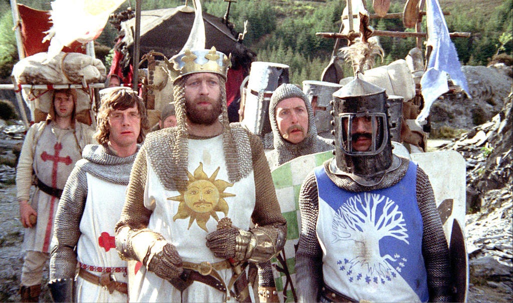 The cast of Monty Python, dressed as Knights of the round table, embarking on their fruitless quest. Eric Idle as Sir Robin sports a particularly ridiculous handlebar moustace.