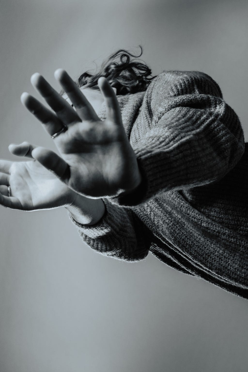Black and white image taken from below of a woman extending her arms toward the camera with her hands outstretched as if she is pushing the camera away.
