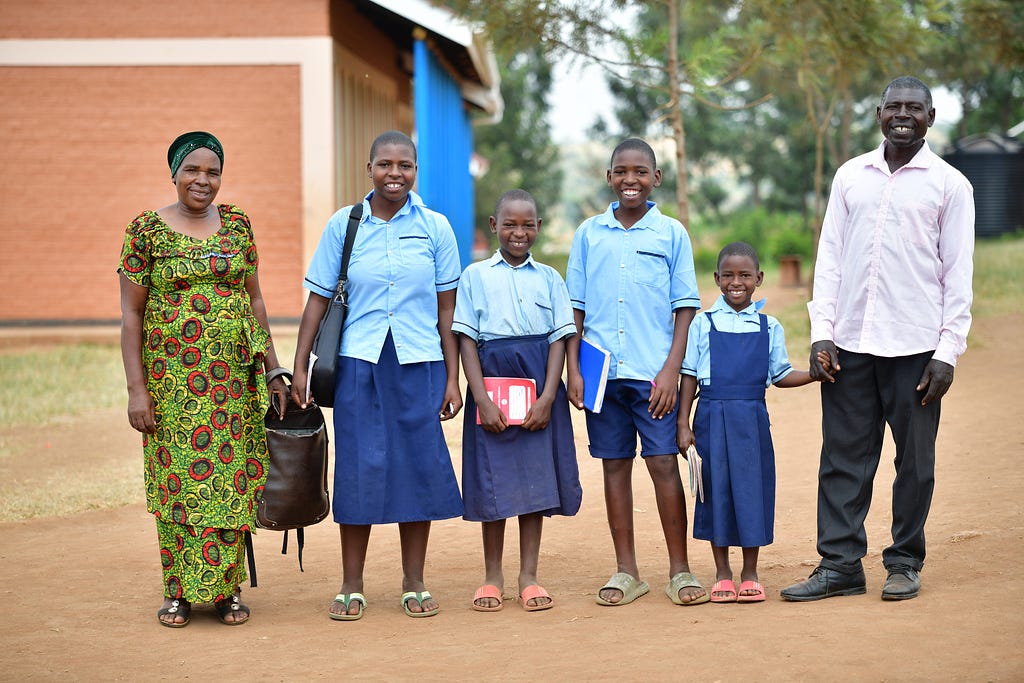 A mother, four of her children dressed in blue school uniforms, and a father stand outside of a school for a family portrait.