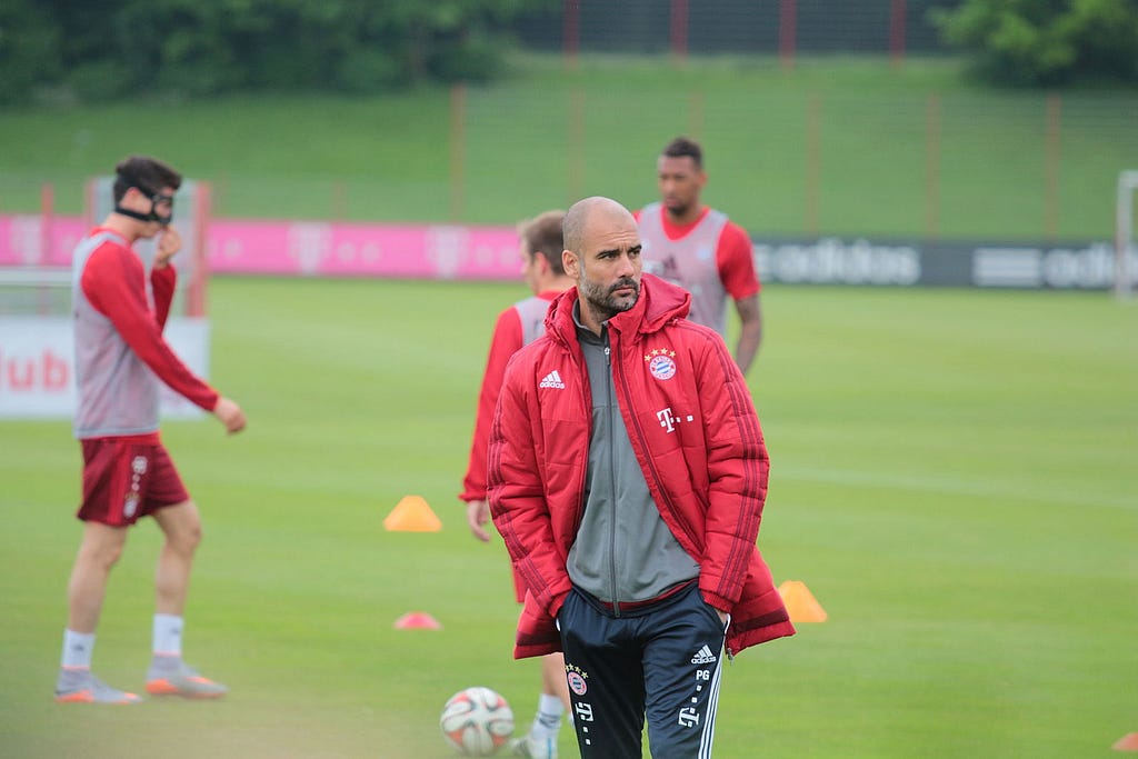 Pep Guardiola in a red jacket, looking to the side with a serious face during a Bayern Munich training session