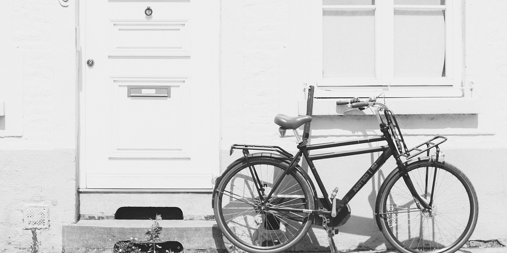 Bicycle outside of a white house wall, in greyscale