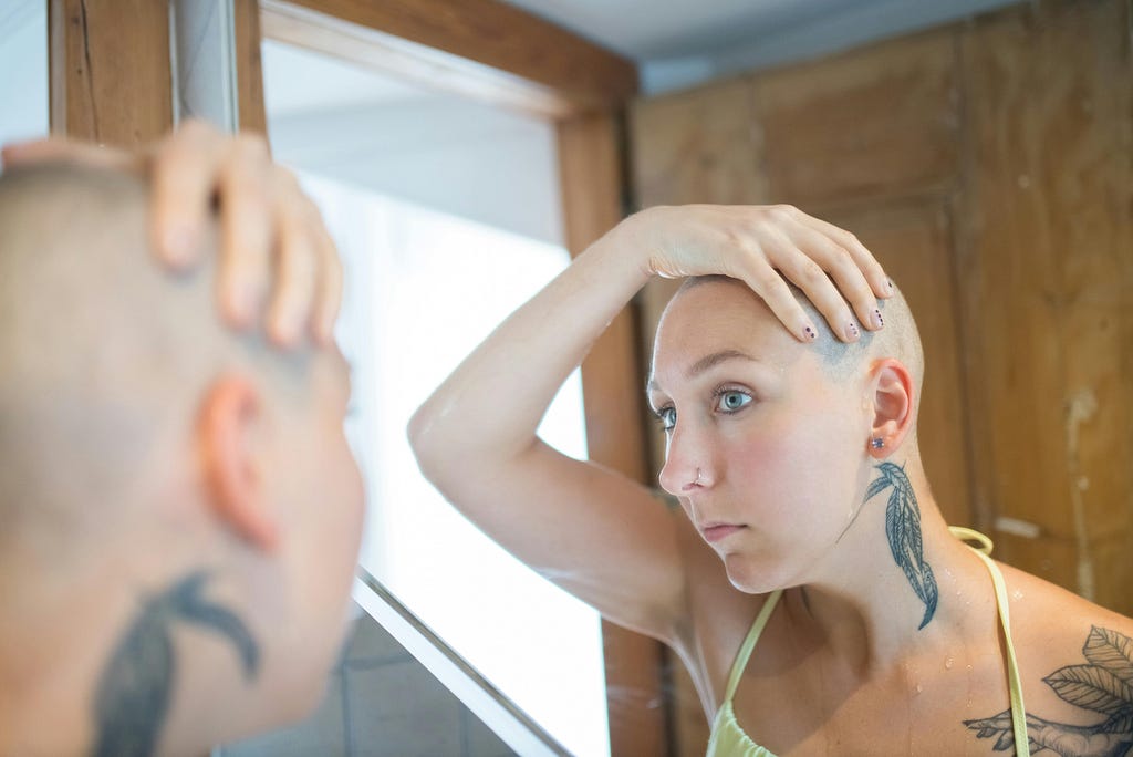 Woman with shaved head looking in the mirror