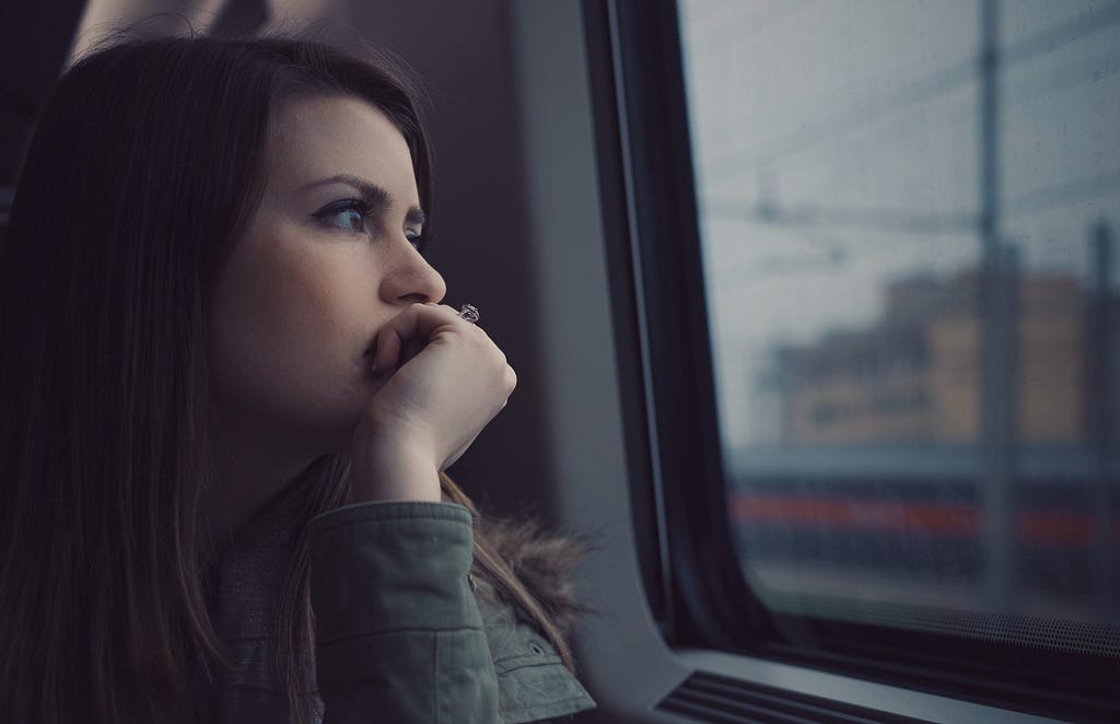 Jeune femme pensive, assise dans un train et regardant par la fenêtre