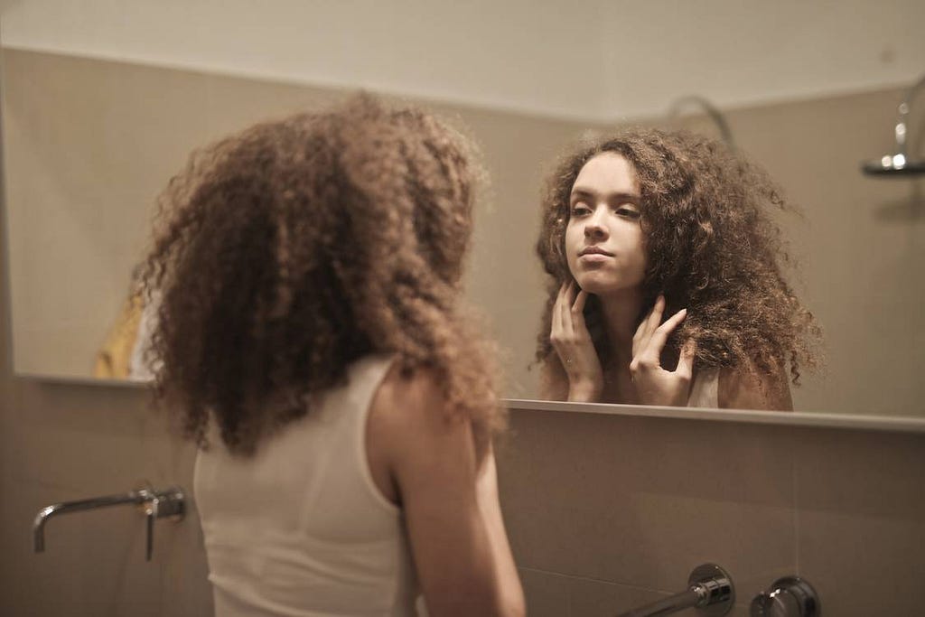 A photo of a woman staring back at herself in the mirror.