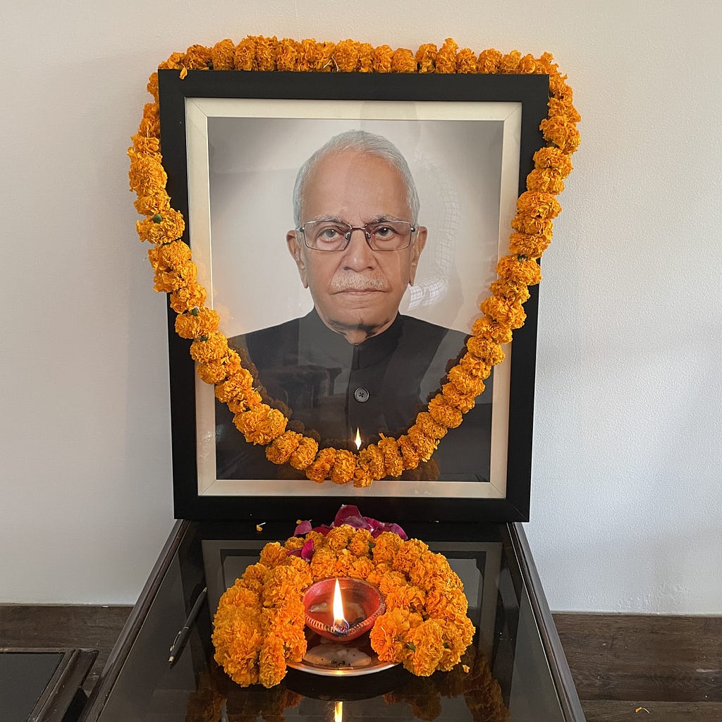 Memorial photo of an older man. Photo is decorated with marigold garland and has marigolds and a candle placed in front of it.