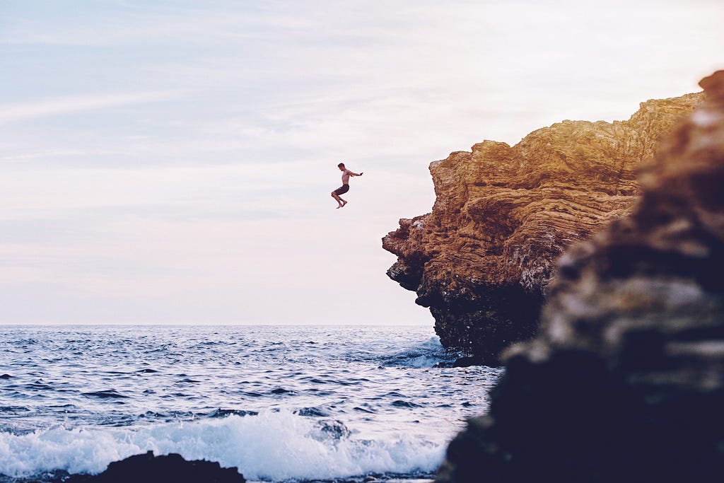 Man jumping off a cliff into the ocean at sunset