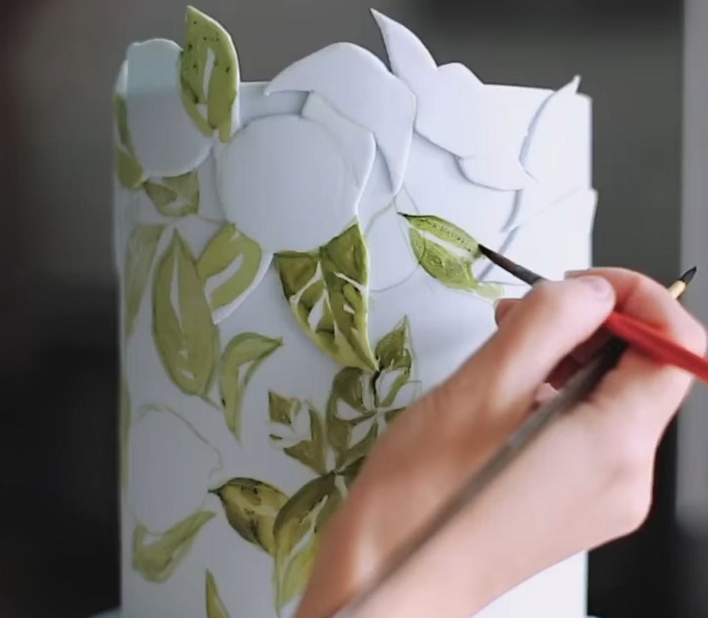 Fotogramma di un video di Tortik che mostra una mano intenta a dipingere una torta