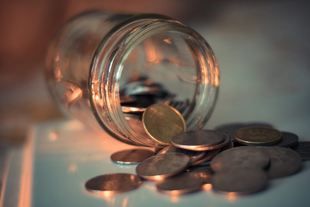 A jar of pennies laying on its side with coins spilling out.