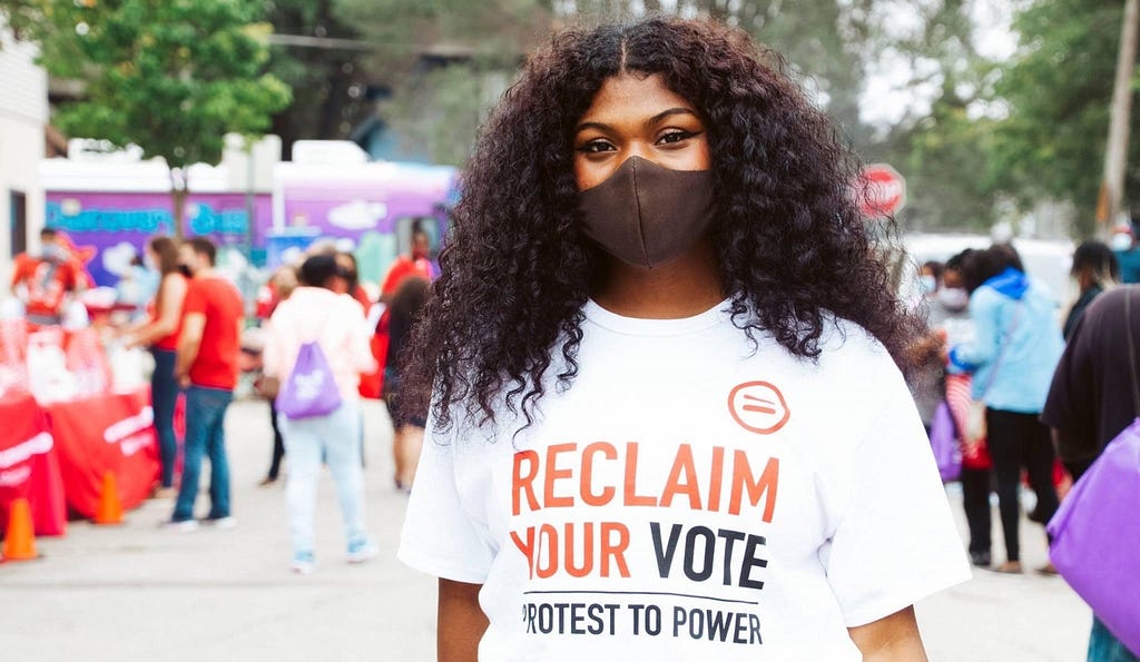 A young person wears a t-shirt that reads, “Reclaim your vote: Protest to power”