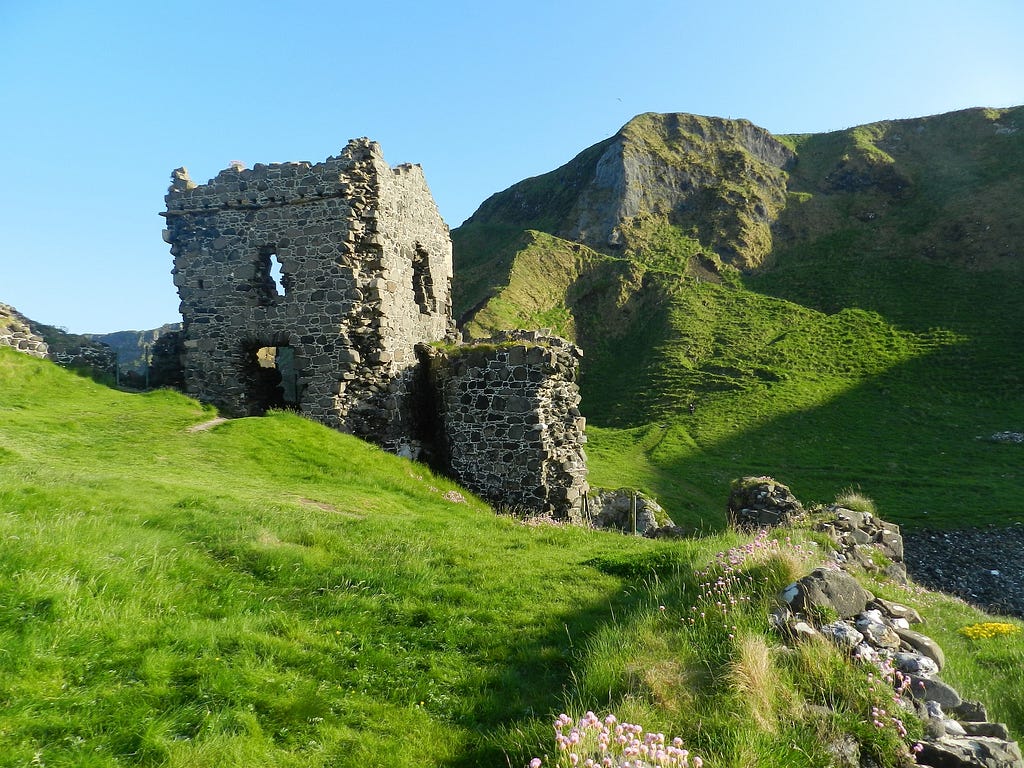 Rolling hills in Ireland, covered with green grass. Ruins of an old castle jut from the hillside.