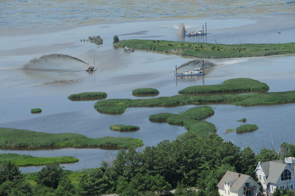 an aerial view of a marsh with several machines launching sediment