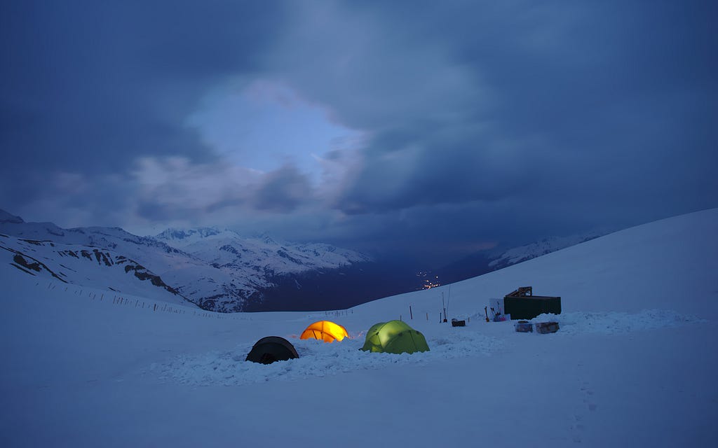 Illuminated tents in twilight at a cloudy, late evening with mountains in the background.