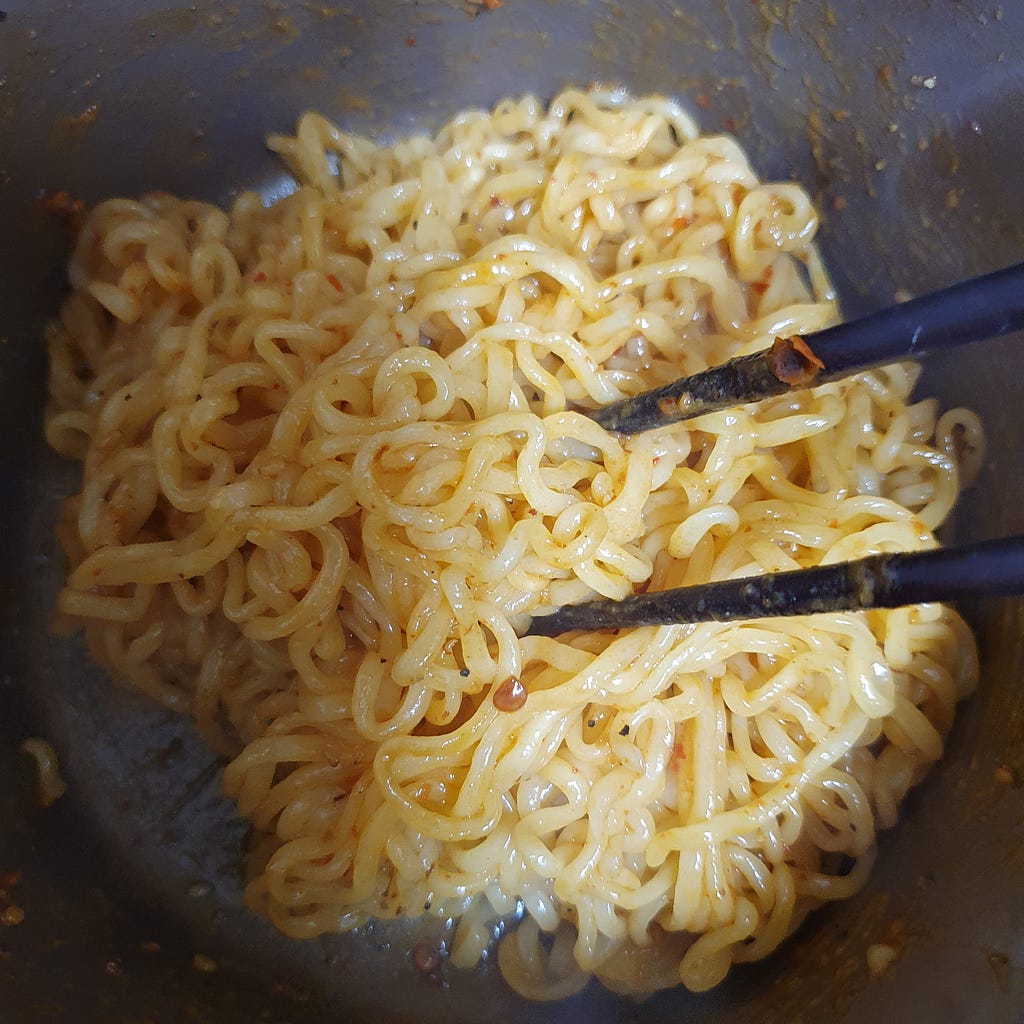 Mixing the noodles well with the bibim sauce for a package of Wicked Ramen (Yogoe Ramyeon) Itaeweon Chamggae Majemat.