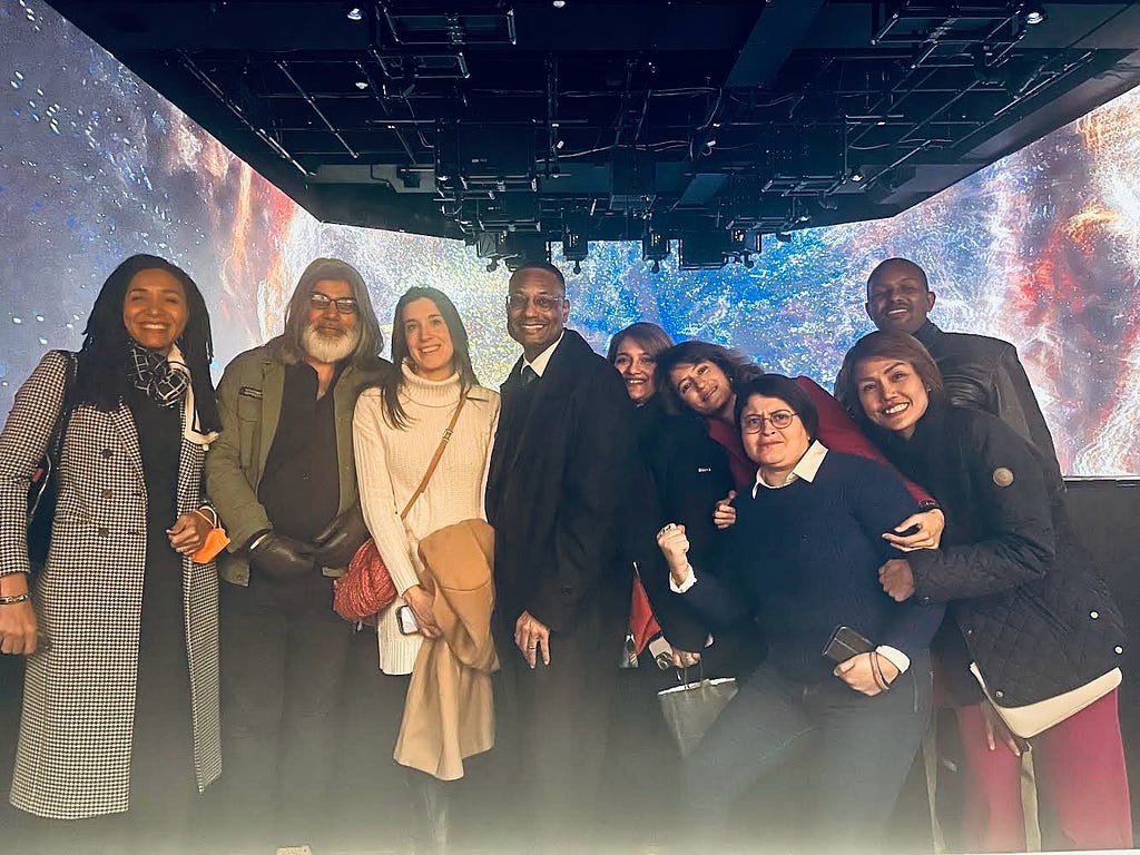A group of people pose for a photo surrounded by an immersive exhibit that makes it appear they are traveling through outer space on the deck of a spaceship.