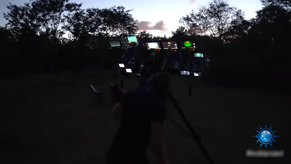 10 cameras mounted to one elaborate tripod film the daytime sky from a grassy area.