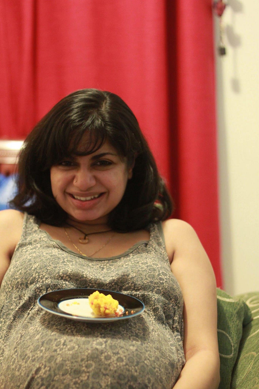 Pregnant Indian woman smiling at the camera with a plate balanced on her belly