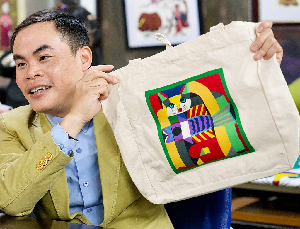 A man holds a tote bag decorated with artwork from the business he founded.