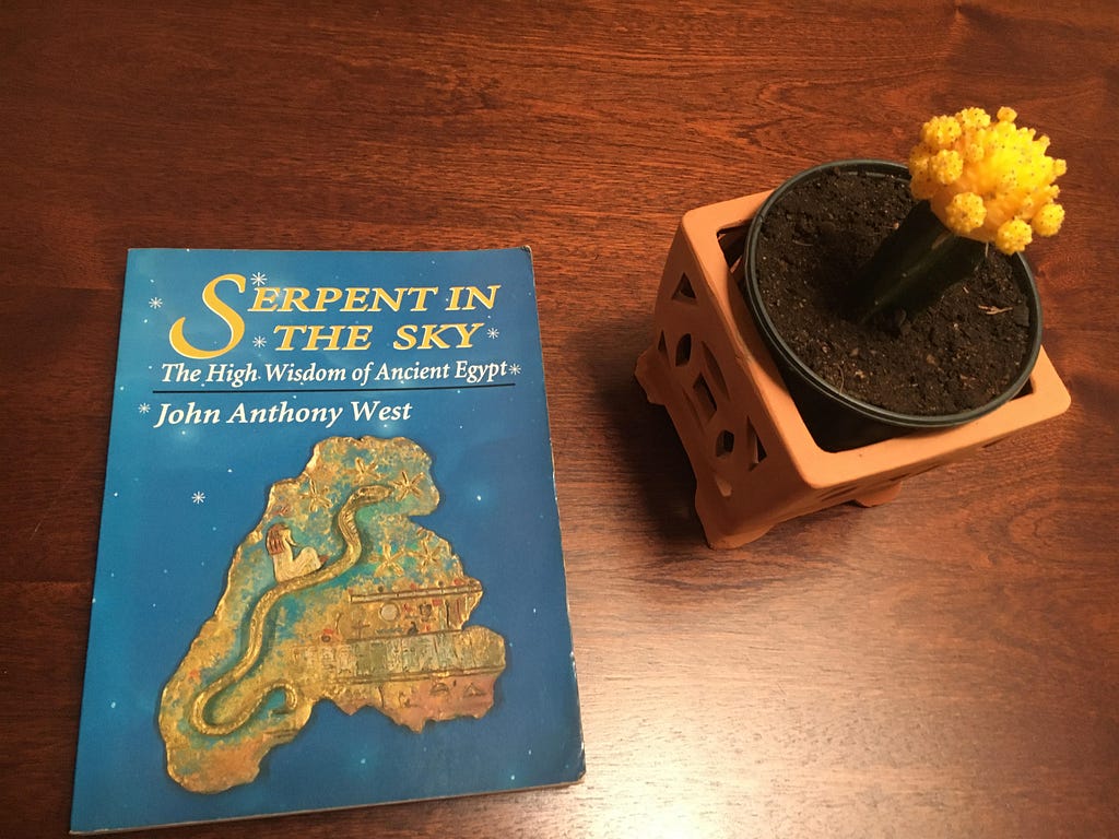 A photo of a book and cactus. The book’s title is “Serpent in the Sky: The High Wisdom of Ancient Egypt” by John Anthony West