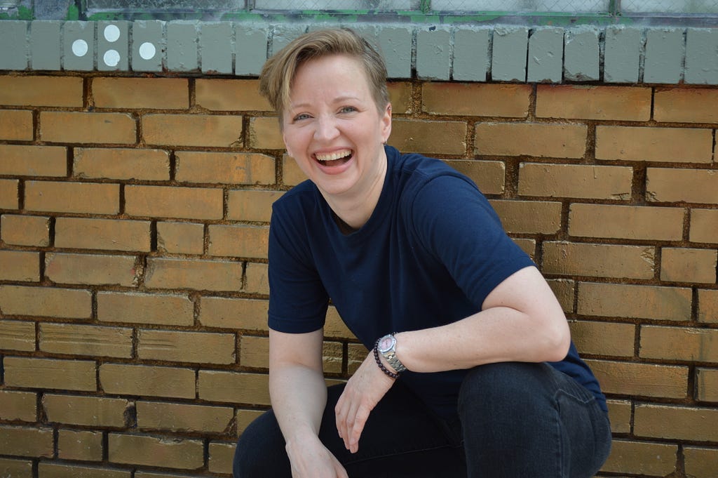 Diane Whiddon laughing, crouched in front of brick wall