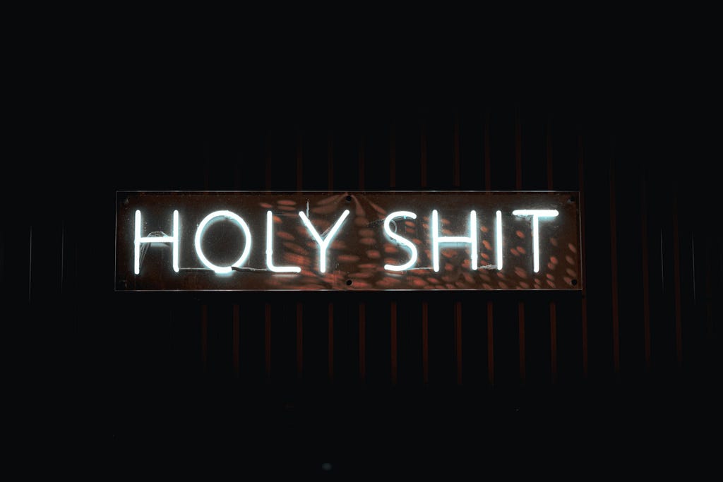 A neon sign saying “HOLY SHIT” on a black background