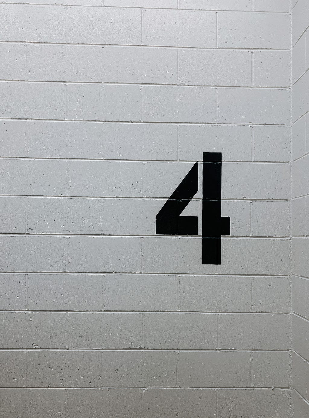 A bold number four on a plain, white brick wall.