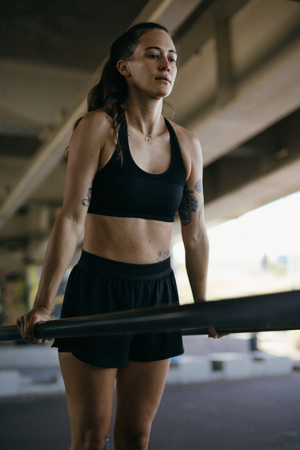 Woman with black sports bra and shorts exercising on a bar in the gym. Her face looks determined.