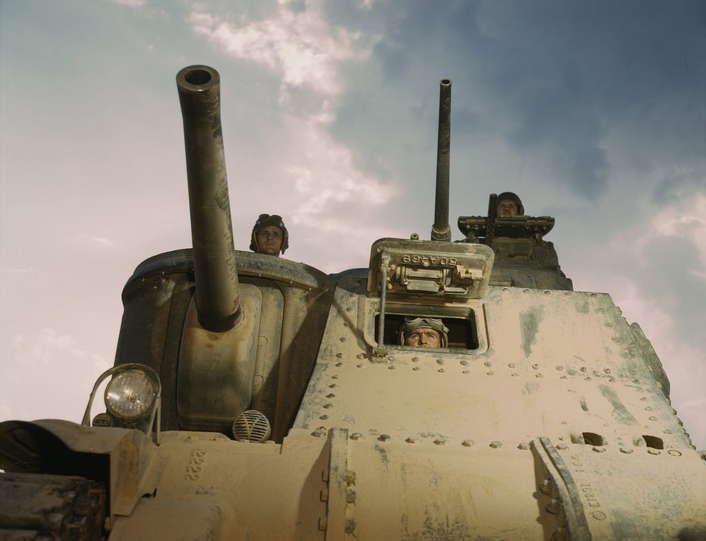 Photo of a tank from the front view, with three crew members inside.
