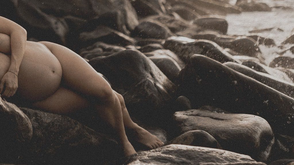 Pregnant woman laying on rocks at the seashore